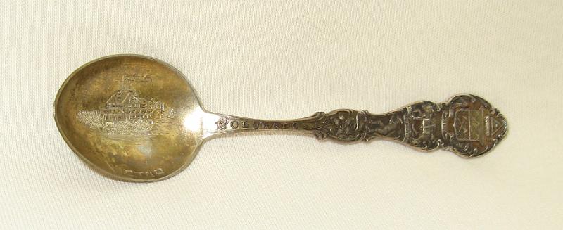 Souvenir Mining Spoon Victor.JPG - SOUVENIR MINING SPOON VICTOR - Sterling silver spoon, 4 1/8 in. long, embossed mining scene in gold-washed bowl with engravedVICTOR for Victor, CO in bowl, handle engraved with various mining scenes, reverse marked Sterling[Victor was founded in 1891, shortly after gold was discovered nearby. The town was named after the Victor Mine, which may have been named for an early settler, Victor Adams. In 1892 Harry, Frank and Warren Woods founded the Mt. Rosa Mining, Milling and Land Company.  Battle Mountain, located just above Victor, had the largest, most prolific mines in the mining district and the town became known as the "City of Mines." Victor officially became a city on July 16, 1894.  In 1894 the Woods brothers discovered gold when they began digging the foundation for a building, which resulted in the creation of the Gold Coin Mine. At that time 8,000 people lived in Victor. The town boomed as the surrounding Cripple Creek mining district quickly became the most productive gold mining district in Colorado. Mines in Victor and Cripple Creek provided 21 million ounces of gold. In 2010, the value of the gold would have been more than $10 billion. The mining district, which hit its peak in 1900, became the 2nd largest gold district in the country's history.  Although Victor's fame was overshadowed by that of its neighbor, Cripple Creek, many of the best gold mines of the Cripple Creek district were located at Victor, including Stratton's Independence Mine and Mill and the Portland Mine. Half of Battle Mountain's gold was extracted by the Portland Mine, which was called the 'Queen of the District."  The town declined steadily in the 20th century, as the gold mines became worked out and the cost of mining rose relative to the price of gold (fixed at $20.67/troy ounce).  Area miners enlisted during World War I, and the loss of workers created a steep decline in mining activity to which the area has never recovered.  Gold mining increased in 1934 when the federal government raised the price of gold to $34/ounce, but gold mining was shut down during World War II as nonessential to the war effort. Some mines opened after the war, but all mines in the district closed by 1962.  In 1976 The Cripple Creek & Victor Gold Mining Company was formed as a joint venture to restart mining in the district.  From 1976 to 1989, the company produced 150,000 troy ounces of gold by reprocessing tailings and mining two small surface deposits. The Cripple Creek & Victor Gold Mining Company began the first large-scale open pit mining in the district in 1994.  In 1995 an open pit gold mining operation began on Battle Mountain.  The Cresson mine open pits are located a few miles north of Victor. Mining continues today under the ownership of AngloGold Ashanti, producing about 250,000 troy ounces of gold in 2012.]